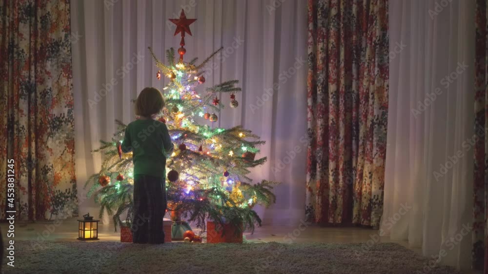 Excited happy cheerful little kid has fun and jump around Christmas tree Excited happy cheerful little kid has fun and jump around Christmas tree