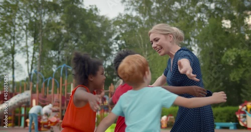 Group of diverse kindergarten students hugging teacher at playground photo