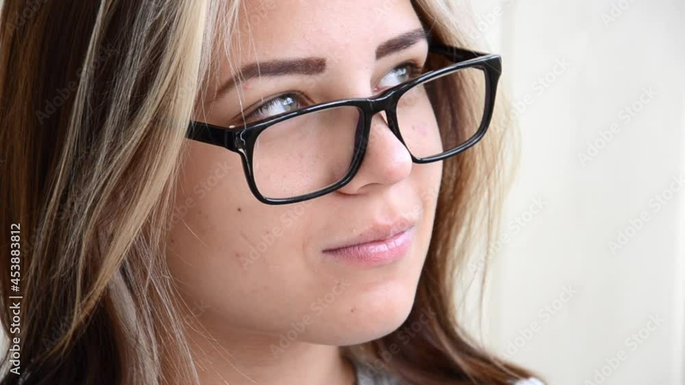 Brunette teen girl with glasses thinks about something. Beautiful caucasian young girl with green eyes looks away and then at camera. Student, entrant or young employee concept. Happy young woman. Brunette teen girl with glasses thinks about something. Beautiful caucasian young girl with green eyes looks away and then at camera. Student, entrant or young employee concept. Happy young woman.