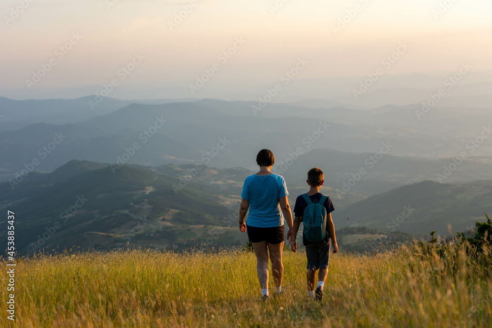 family travel concept- mother and son hiking in mountains. Mother and daughter watching the sunset on the lake. Travel with children, The kid holds mom's hand, Mountain trail.
