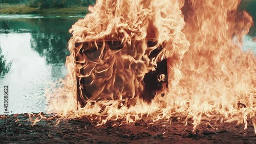 Retro vintage TV set against the background of river explodes beautifully with clouds of fire. Water is also burning. Concept of post apocalypse, surrealism and fire hazard of old worn out equipment