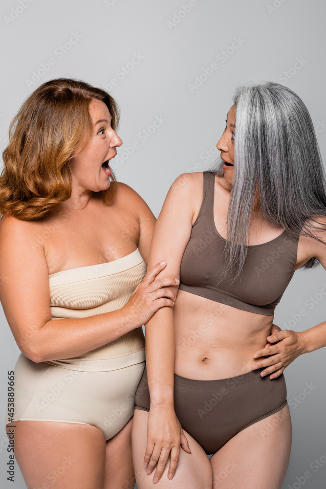 Excited woman in lingerie hugging asian friend isolated on grey, body  positive concept Photos | Adobe Stock