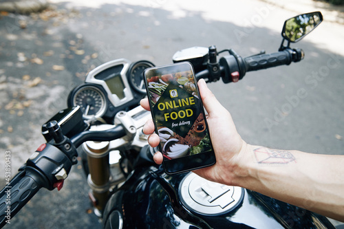 Hand of man sitting on motorcycle showing food delivery application on smartphone