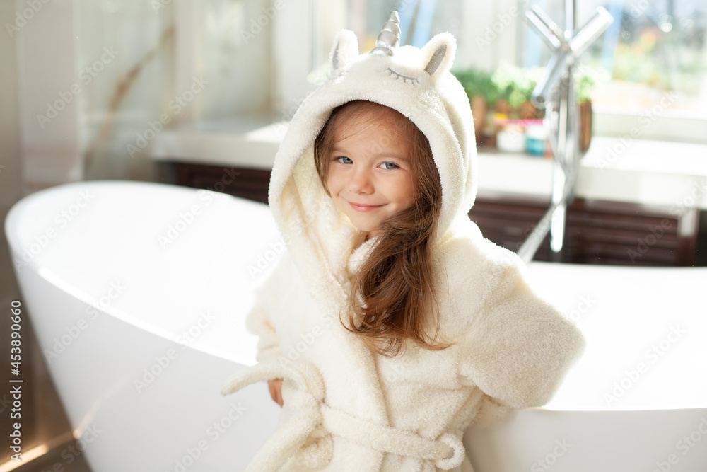Portrait of a cute girl in a white coat with a unicorn in a bright bathroom with a window. Hygiene. Morning routine. Purity. Portrait of a cute girl in a white coat with a unicorn in a bright bathroom with a window. Hygiene. Morning routine. Purity.