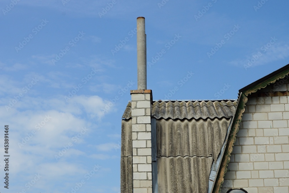 one long chimney on a gray slate roof of a rural house against a blue sky one long chimney on a gray slate roof of a rural house against a blue sky