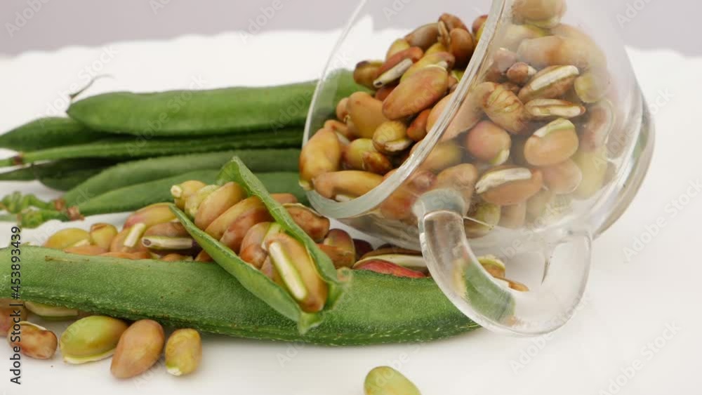 Rotating shot of transparent glass filled with seeds of beans and green beans isolated over white plate Rotating shot of transparent glass filled with seeds of beans and green beans isolated over white plate