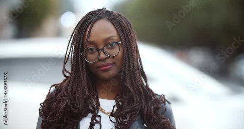 Bokeh shot of afrian young woman looking at camera standing under rain on city street photo