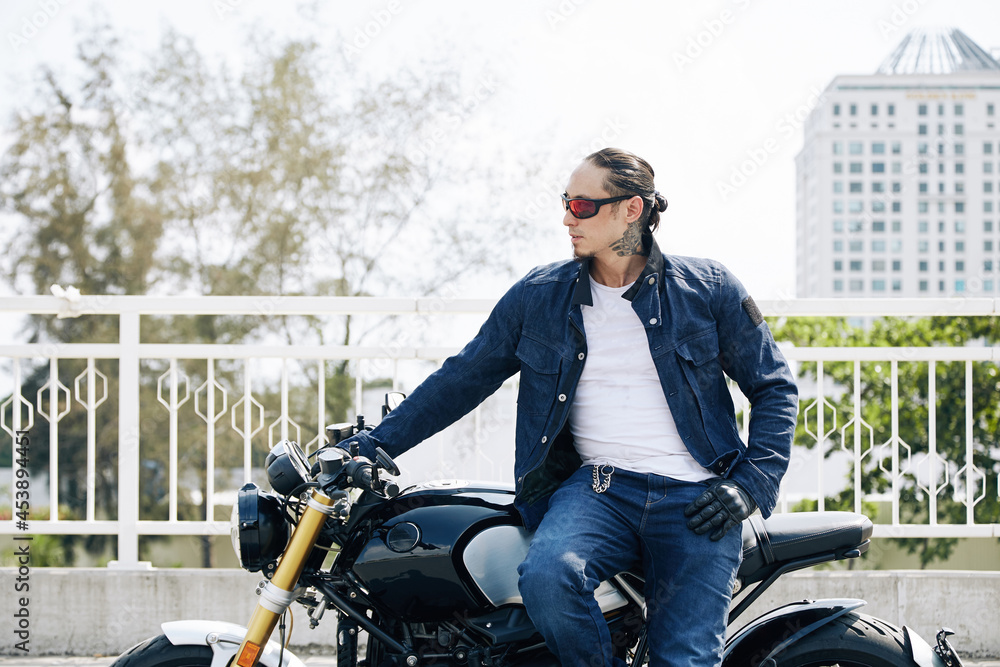 Stylish confident man in sunglasses sitting on motorcycle and looking away