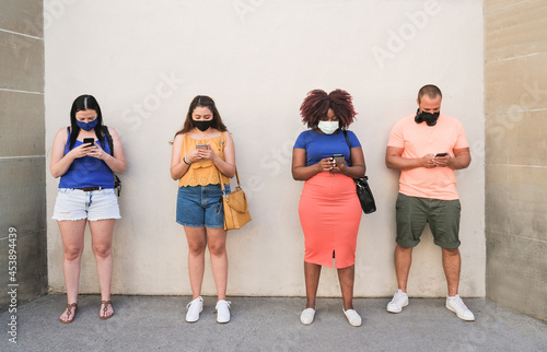 Group of multiracial friends using mobile phones in the city while standing with social distance and wearing safety face mask for coronavirus outbreak