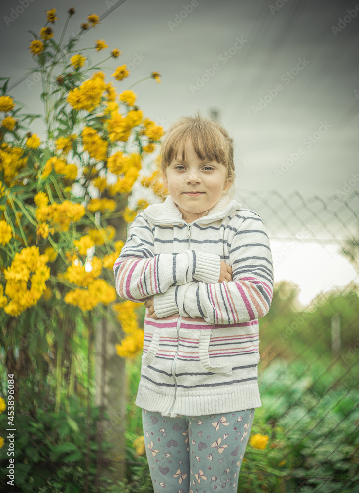 a small blonde girl stands against a background of yellow flowers a small blonde girl stands against a background of yellow flowers