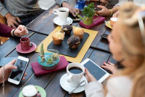 group of people with eating muffins and drinking coffee at breakfast, young people at table, focus on food and smartphone, breakfast, technology and friendship concept