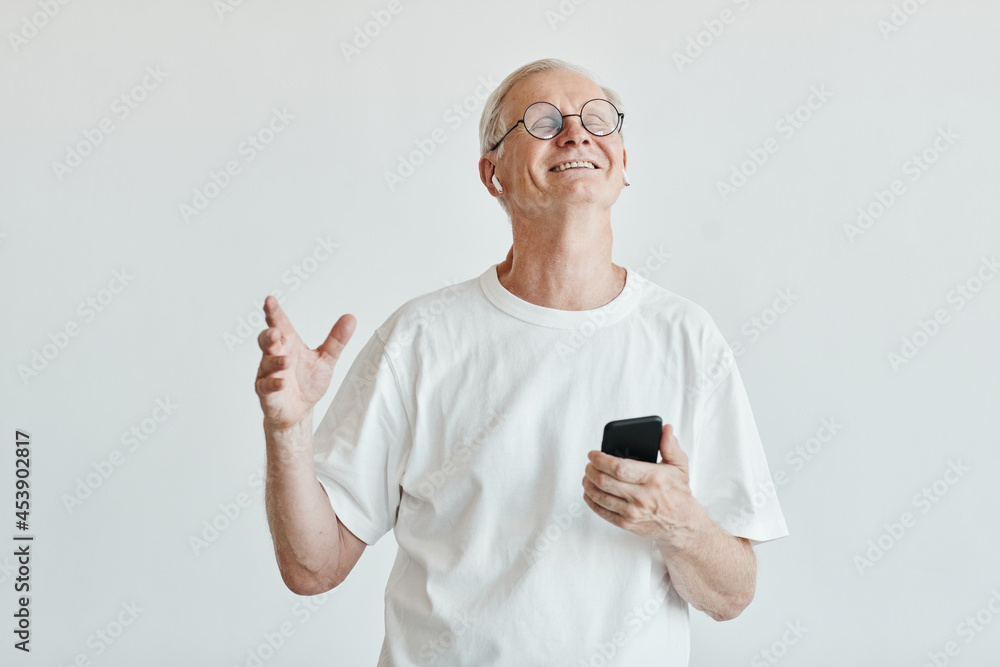 Minimal waist up portrait of smiling senior man dancing and holding smartphone against white background Minimal waist up portrait of smiling senior man dancing and holding smartphone against white background