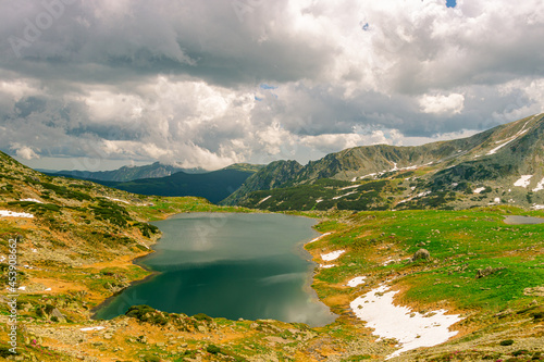 Beautiful view of a glacial lake in the mountains under cloudy sky. View of Bucura lake located in Retezat mountains in Romania. View of a mountain lake in a rainy day.