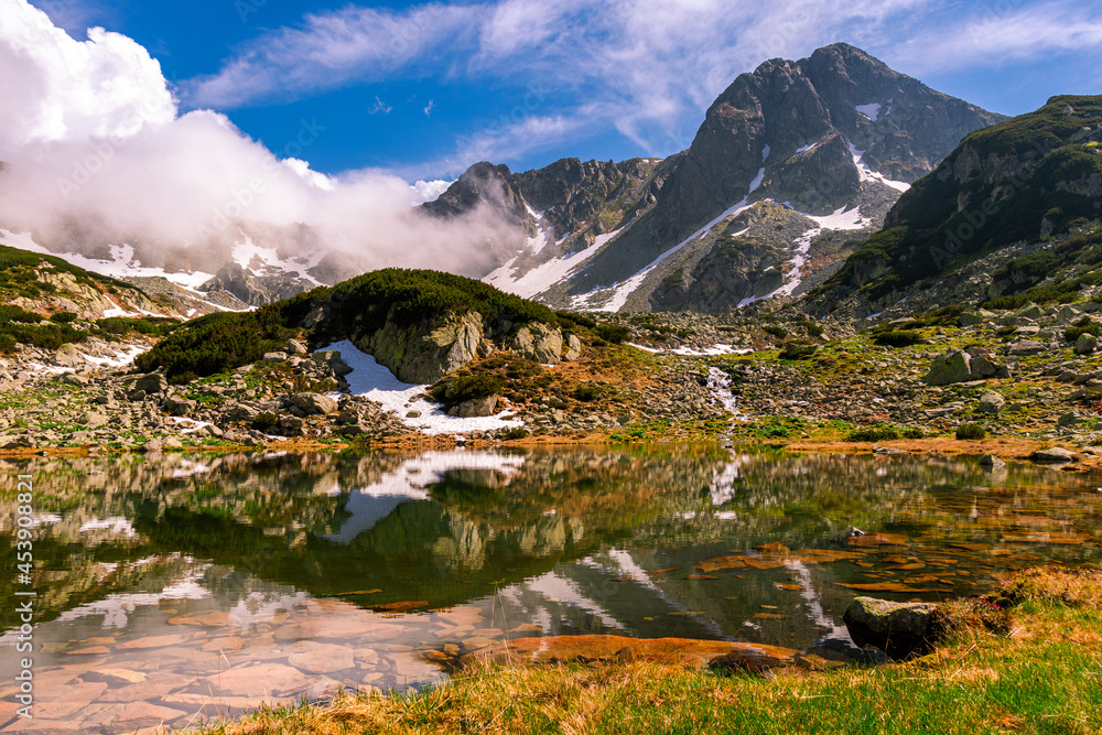 Glacial lake in the mountains landscape in summer. Lovely landscape photography of a mountain lake with mountain peaks in the background. Weather is sunny with a couple pf clouds. 