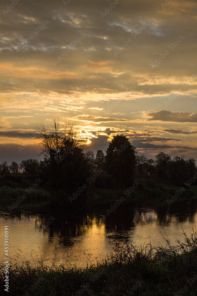 A beautiful sunrise over the river and black silhouettes of trees against the background of a cloudy dramatic sky in the early summer morning and a space to copy