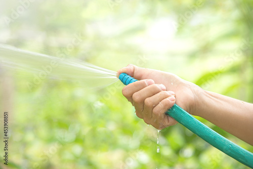 Hand holding rubber water hose and using finger close end of the rubber hose to make to water spray .Green bokeh background.