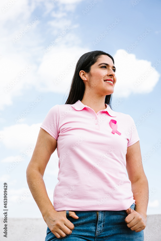 portrait of latin woman hand holding pink breast cancer awareness ribbons with blue sky as background in Latin America portrait of latin woman hand holding pink breast cancer awareness ribbons with blue sky as background in Latin America