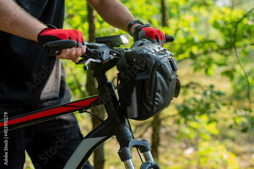 A cyclist in gloves near a mountain bike with a bag on the handlebars.