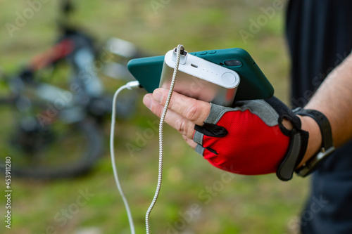 Man charges a smartphone with a power bank on the background of a bicycle in the forest.