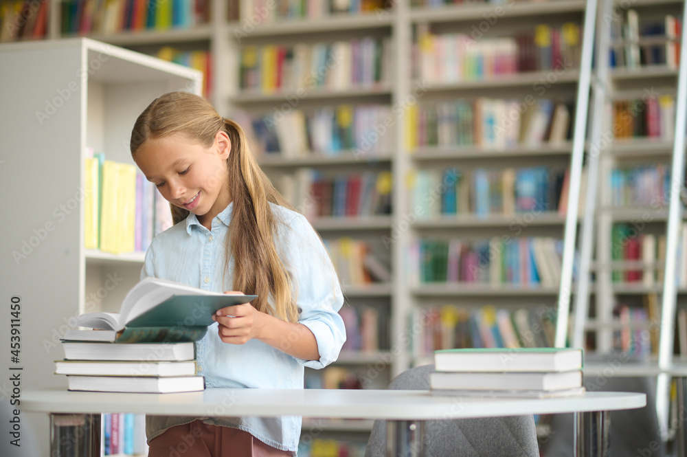 Joyful pupil reading a textbook at the library desk Joyful pupil reading a textbook at the library desk