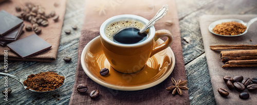 A cup of aromatic black coffee, a coffee maker, coffee beans of different varieties on the table. Morning espresso or Americano coffee for breakfast in a beautiful brown cup.