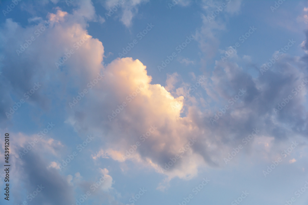 Evening blue sky with clouds at sunset. Clouds are illuminated by the rays of the setting sun.