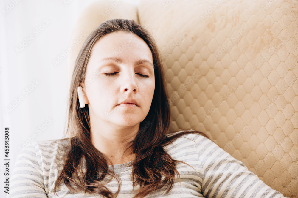 Beautiful brunette girl sitting in armchair with wireless headphones. Young woman with her eyes closed resting and listening to music or audiobook. Beautiful brunette girl sitting in armchair with wireless headphones. Young woman with her eyes closed resting and listening to music or audiobook.