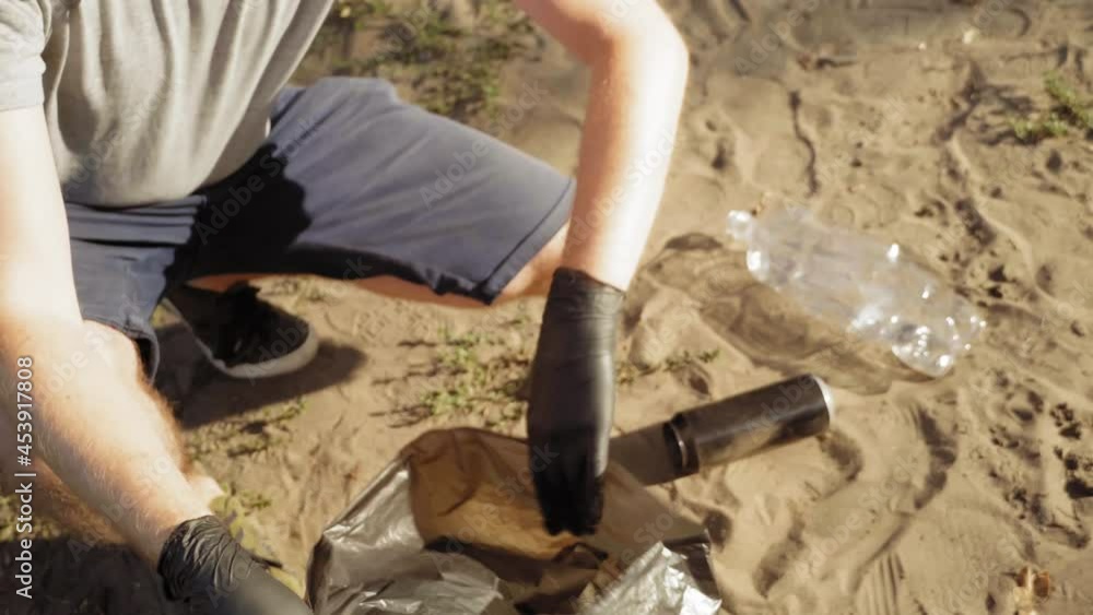 Man picking up bottle into garbage bags while cleaning area in park. Volunteering, charity, people, ecology concept Man picking up bottle into garbage bags while cleaning area in park. Volunteering, charity, people, ecology concept