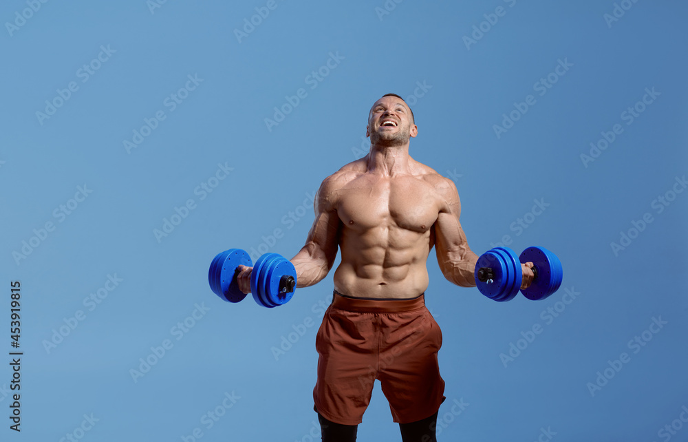 Male muscular athlete with dumbbells in studio