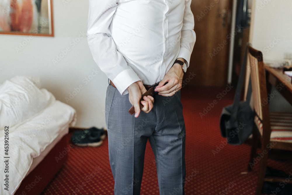 Fototapeta premium Groom getting ready, putting on a belt on his wedding day