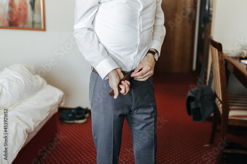 Groom getting ready, putting on a belt on his wedding day