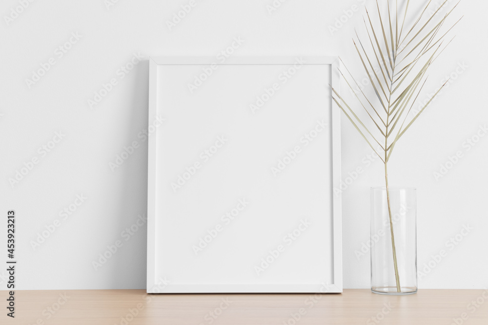 White frame mockup with a palm leaf on the wooden table. White frame mockup with a palm leaf on the wooden table.