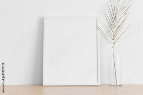 White frame mockup with a palm leaf on the wooden table.