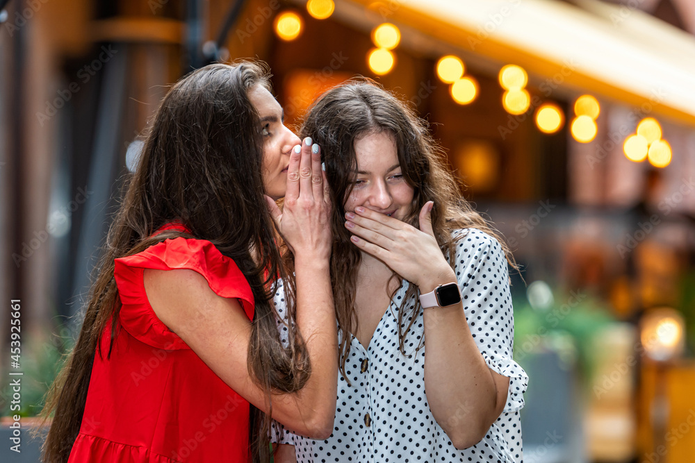 two young women whispering and smiling,  sharing their secrets, street lights background