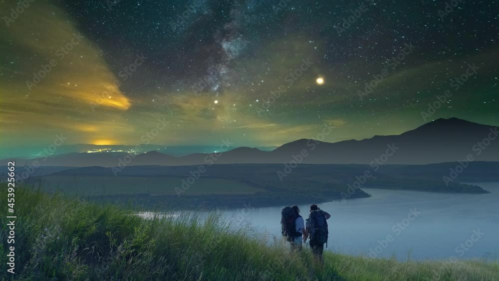 The two travelers standing on mountain top on beautiful starry sky background The two travelers standing on mountain top on beautiful starry sky background