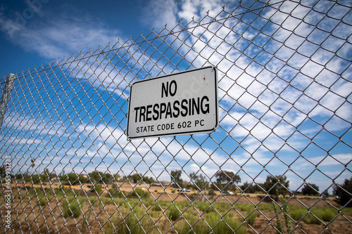 A sign stating No Trespassing on a chain link fence against a blue sky with negative space