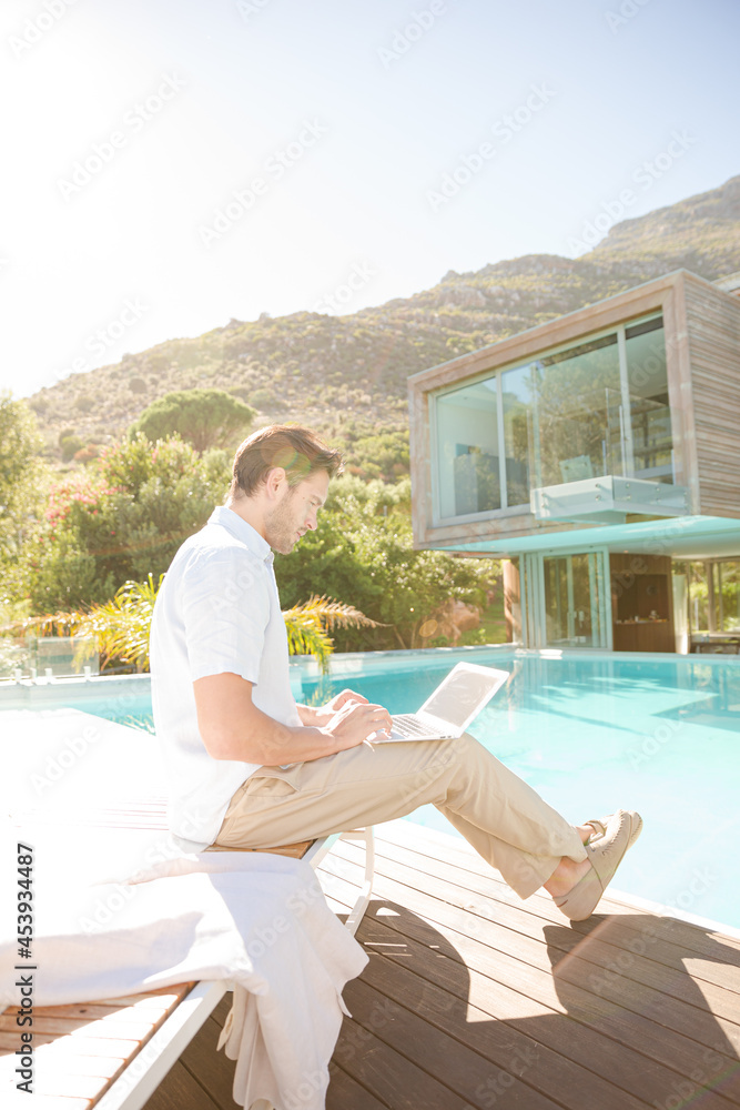 Fototapeta premium Man using laptop at poolside