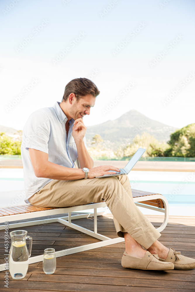Man using laptop on lounge chair at poolside