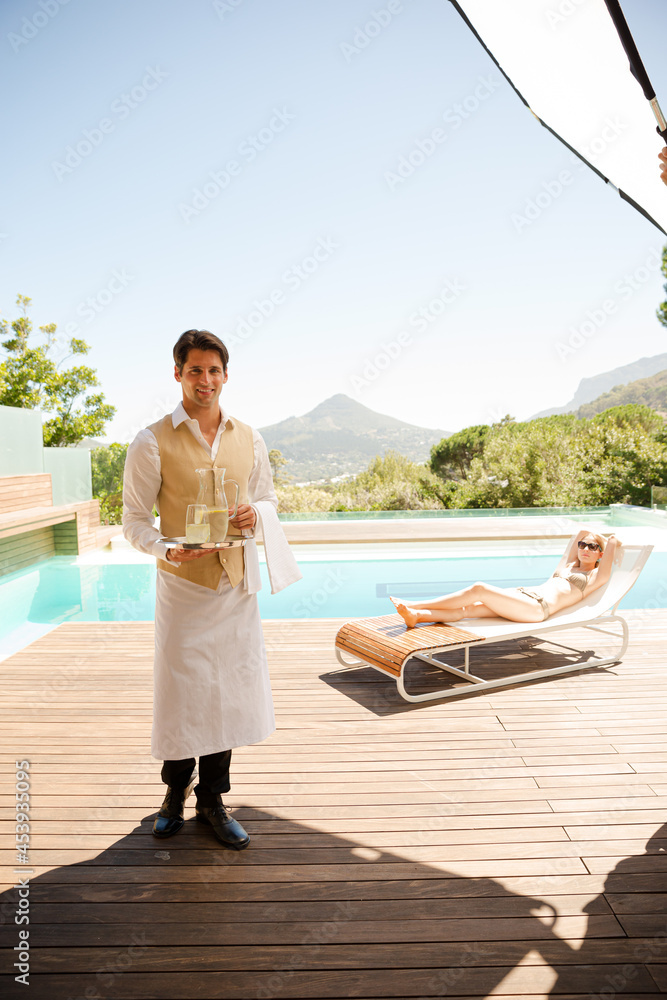 Waiter serving woman on lounge chair at poolside