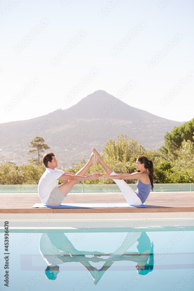 Couple practicing yoga at poolside