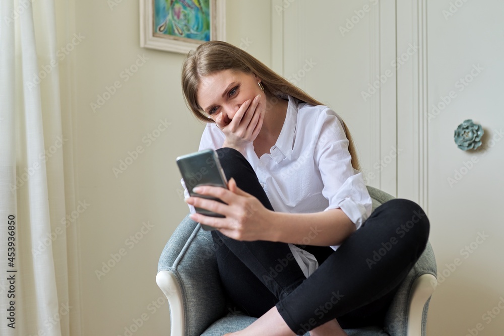 Emotional young beautiful woman looking at smartphone screen