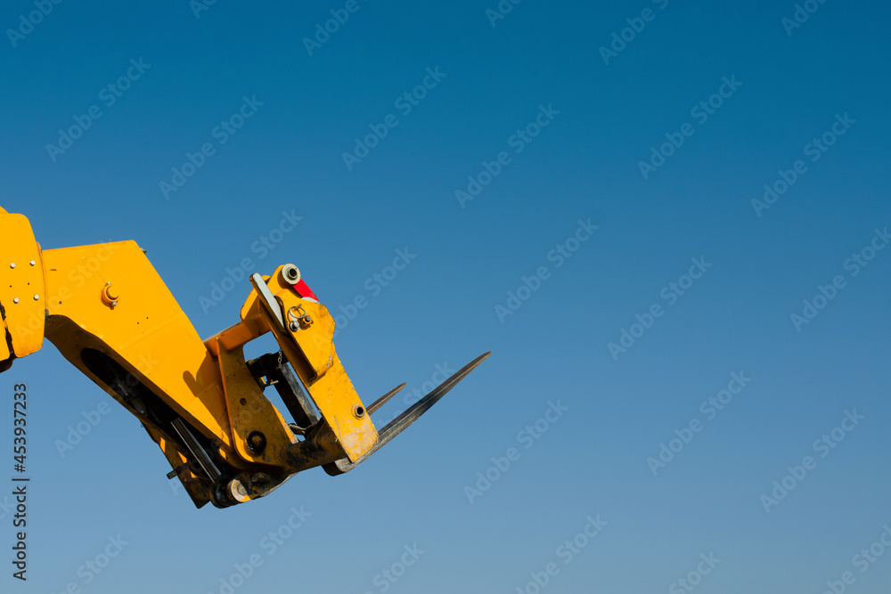 Forks of the Telescopic Forklift Telehandler raised on the blue sky background Space for text Forks of the Telescopic Forklift Telehandler raised on the blue sky background Space for text