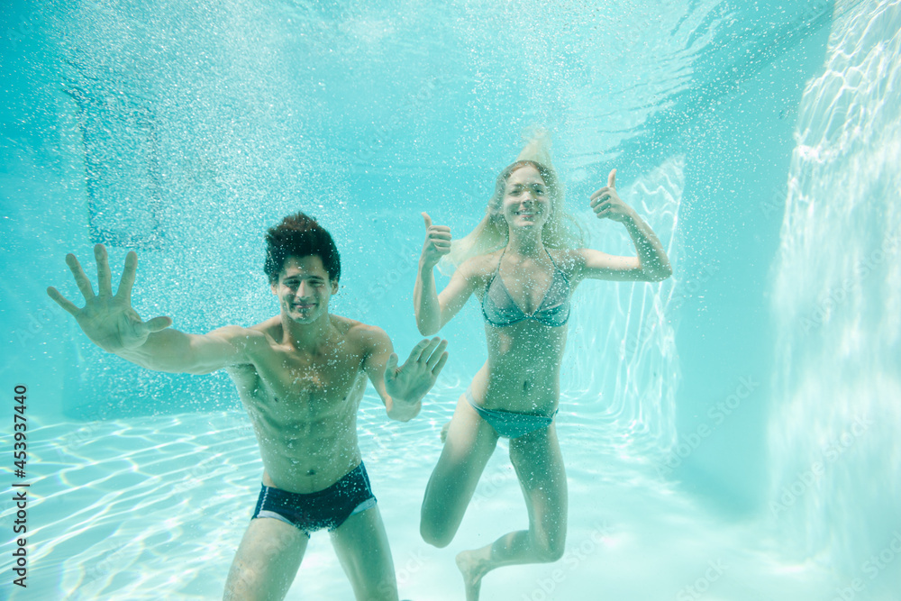 Couple giving thumbs up underwater in swimming pool