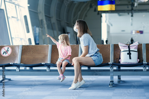 Mother with daughter in masks waiting for their flight at airport. Woman with little girl in international airport.