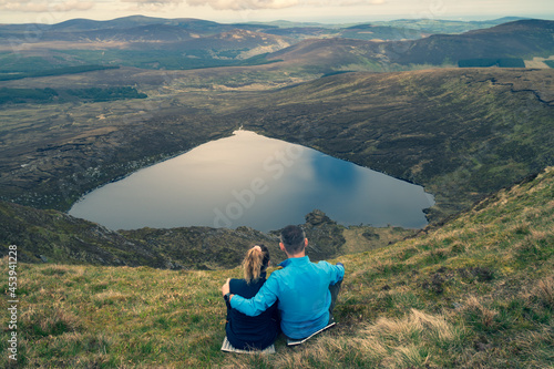 Couple sitting on the top of the mountain. View from behind.. Heart shaped Lake Ouler Tonelagee Mountain, Wicklow County, Ireland. photo