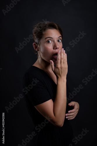 A young beautiful woman surprised by something in a studio shot in black dress and background © Dellealpi