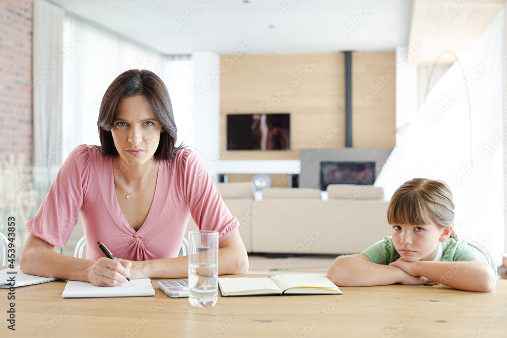 Woman sitting at table with daughter, using calculator