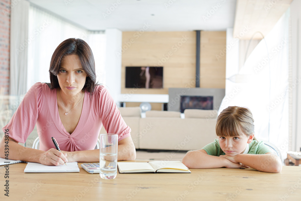Mother sitting at table with daughter, using calculator