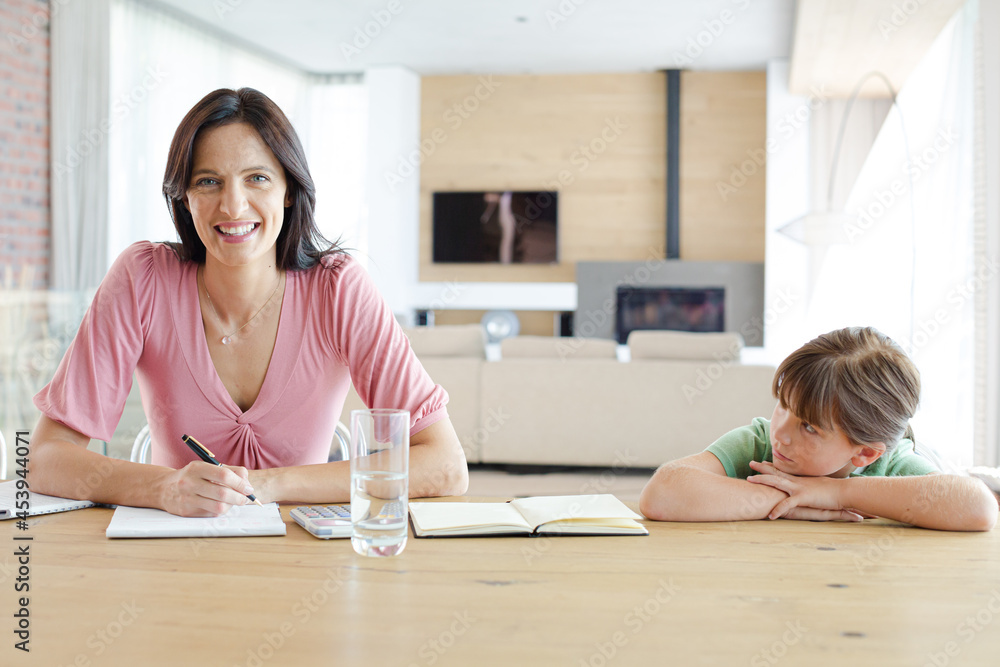 Woman sitting at table with daughter, using calculator Woman sitting at table with daughter, using calculator