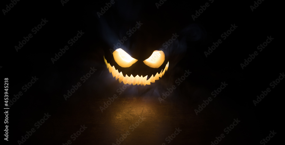 Fototapeta premium Halloween pumpkin smile and scary eyes for party night. Close up view of scary Halloween pumpkin with eyes glowing inside at black background